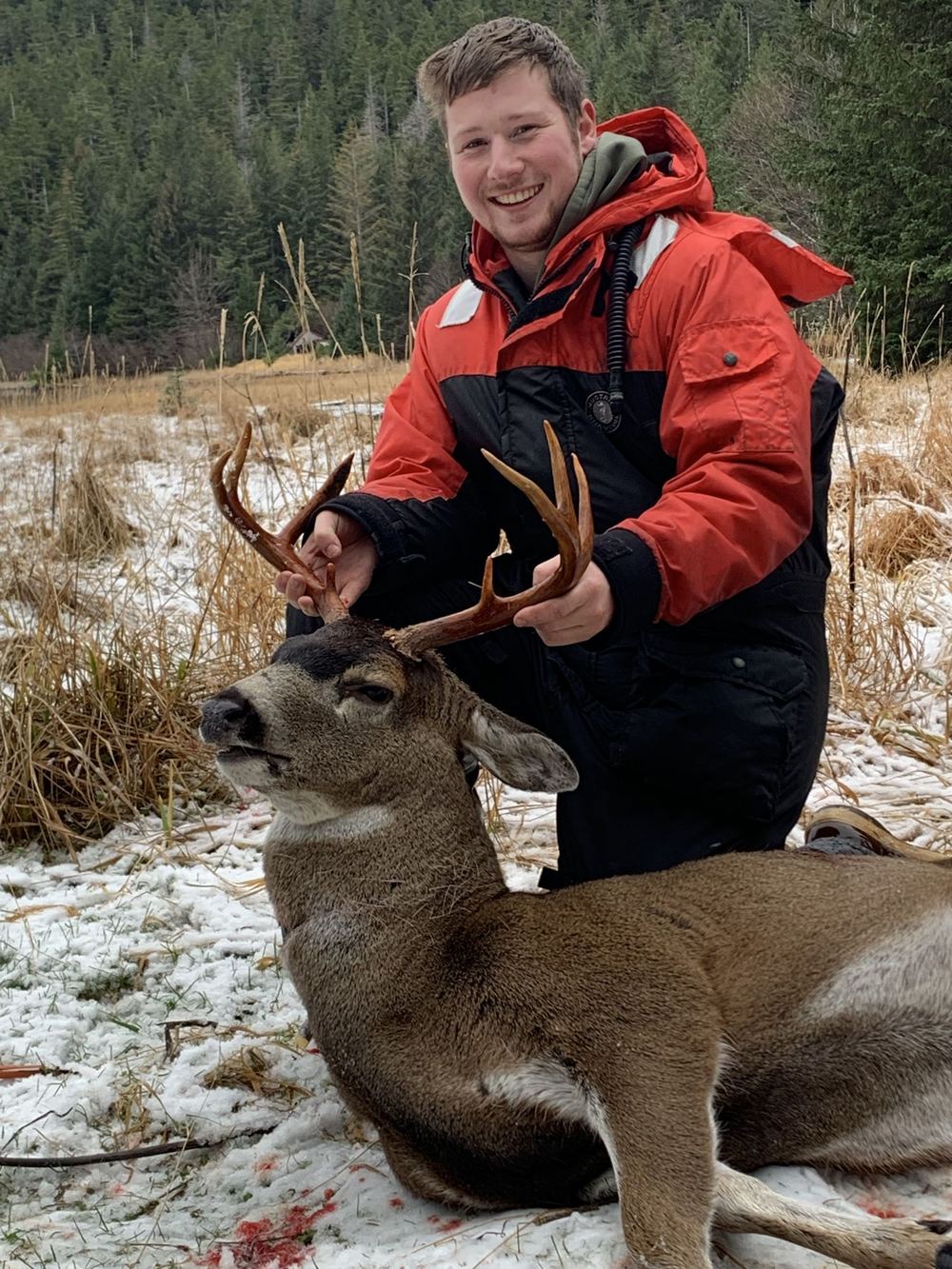 Hunter with a blacktail deer in early-winter snow near Sitka